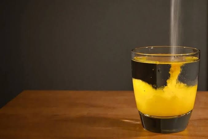 Yellow powder clouding through water against a dark background