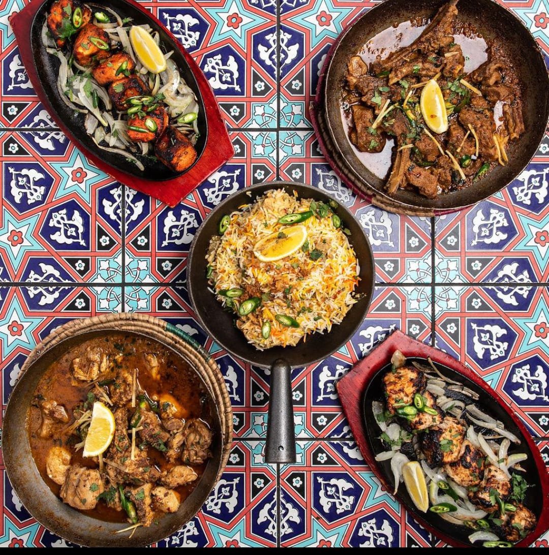 Top-down spread of spiced grilled and curried dishes on patterned tile